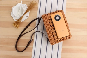 Detailed overhead shot of a beige woven straw crossbody bag with dark brown leather strap
