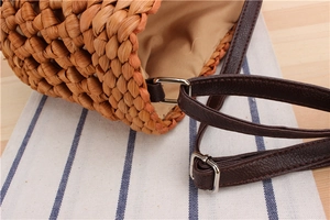 Detail of woven straw bag texture with brown leather strap and metal buckle on wooden table