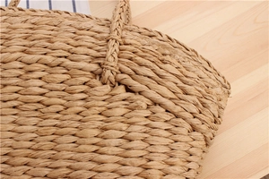 Detailed view of reinforced handle joints on natural woven straw shoulder bag