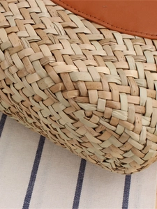 French style woven straw handbag with brown leather trim on striped background