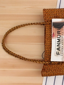 Handmade forest style woven straw shoulder bag in caramel brown on a rustic wooden table