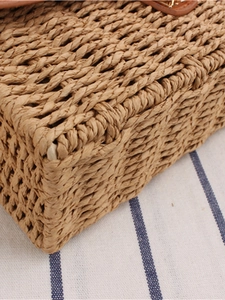 Close-up of woven straw tote bag with brown leather clasp and metal hardware