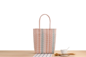 Detailed cross-weave texture of pink and blue striped plastic woven tote bag on a table