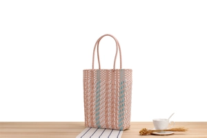 Detail of pink and blue striped plastic woven basket bag on a minimalist wooden table