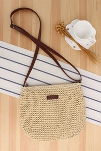 Detailed view of handmade woven paper straw bag with brown leather strap and wood texture