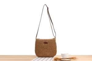 Detail of woven straw crossbody bag with brown leather strap on a cafe setting table