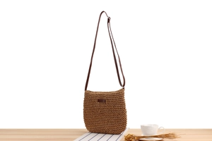 Detailed close-up of woven paper rope texture and leather brand patch on brown crossbody bag