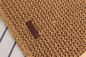Close-up of woven paper straw texture with brown leather patch detail on a crossbody bag
