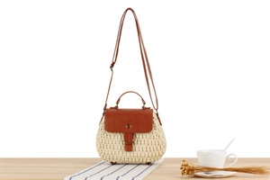 Detail of handmade straw bag with brown leather trim and ring decor on wooden table