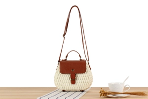 Close-up of straw woven crossbody bag with brown leather flap and round metal buckle