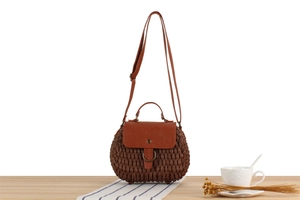 Detail of woven straw crossbody bag with brown leather flap and metal ring on wooden table