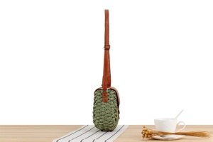 Detail of green woven crossbody bag with brown leather flap and adjustable strap