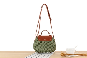 Detail of green woven handbag featuring brown leather flap and adjustable shoulder strap