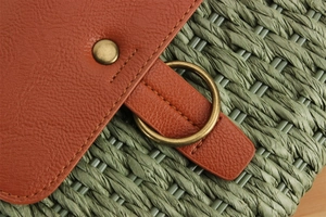 Detail of green woven straw bag featuring brown lychee leather flap and brass ring buckle