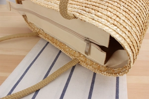 Detail of woven straw tote bag with fabric lining, zipper closure and rope handles