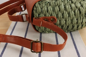 Close-up of green straw weave texture with brown leather strap and bronze metal rivets