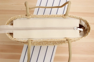 Detail of woven straw beach bag featuring beige canvas lining and smooth metal zipper closure