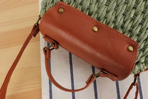 Detail of green straw woven texture and brown leather flap with metal rivets