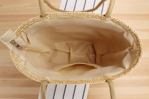 Detail of straw tote bag interior featuring fabric lining, inner pocket, and zipper closure