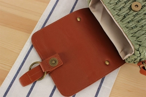 Detail of green woven straw bag featuring brown leather flap and bronze magnetic clasp