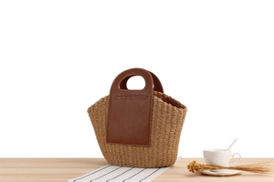 Detail of paper rope woven tote with brown leather patch and stitching on wooden table