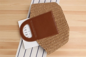 Detail of hand-woven straw tote with brown leather handles and contrast stitching