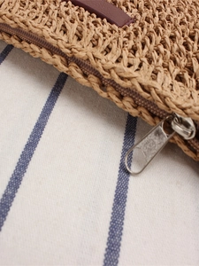 Handwoven straw crossbody bag with brown leather trim and zipper on striped fabric
