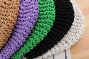 Macro detail of hand-woven cotton bucket bags in five vibrant colors on a wooden table