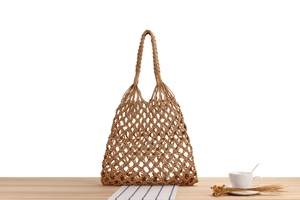 Detailed knit texture of a beige hollow woven tote bag on a wooden table setup