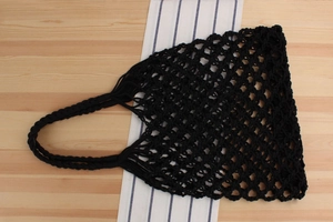 Detail of handwoven black cotton mesh tote bag with reinforced handles on wooden table