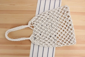Detail of beige macramé woven tote bag with textured diamond mesh and braided handles