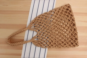 Close-up of khaki woven cotton net bag showing hollow mesh texture and braided handle