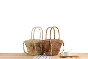 Détail du sac à bandoulière en paille tissée avec pompon et perles sur table en bois