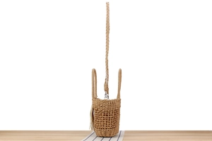Détail macro d'un sac seau en paille tissé main avec pompons et motif ajouré complexe