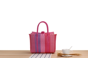 Detail of pink hand-woven beach bag with blue stripes on a wooden surface