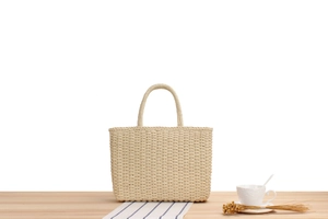 Détail d'un sac cabas tissé beige sur une table en bois avec une ambiance de vacances