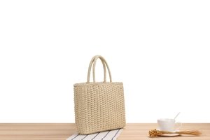 Détail d'un sac cabas en paille tressée crème avec texture crochet sur table bois