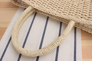 Détail de la poignée du sac en paille tressée montrant la texture et la doublure en soie