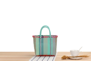 Close-up of mint green woven picnic basket with colorful stripes on a wooden table