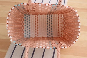 Top view of handwoven peach pink plastic picnic basket with blue and white accents
