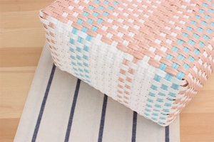 Detailed top view of pastel pink, blue, and white woven picnic basket on a light wood surface