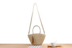 Detail of hand-woven straw crossbody bag with fringe tassel and pearl on wooden table