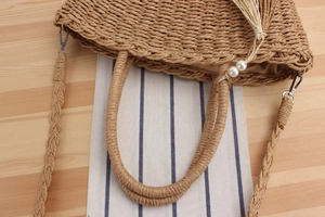 Detail of woven straw bag showing pearl charm, fringe tassel and detachable strap