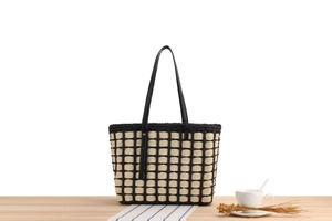 Detail of hand-woven checkerboard tote bag with black straps on a wooden surface