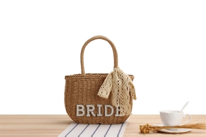Detail of woven straw tote bag with pearl BRIDE lettering and lace scarf handle