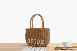 Close-up of woven straw handbag with BRIDE pearl lettering for beach weddings