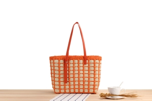 Detail of orange woven tote bag showing texture and leather straps on a styled tabletop