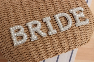 Close-up of handmade straw clutch featuring BRIDE pearl lettering and rhinestone details