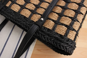 Detail of woven straw tote featuring black leather strap with silver rivet accents
