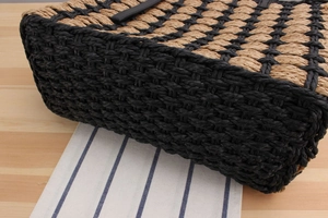 Detail of hand-woven straw tote bag with black and yellow diamond pattern and leather strap